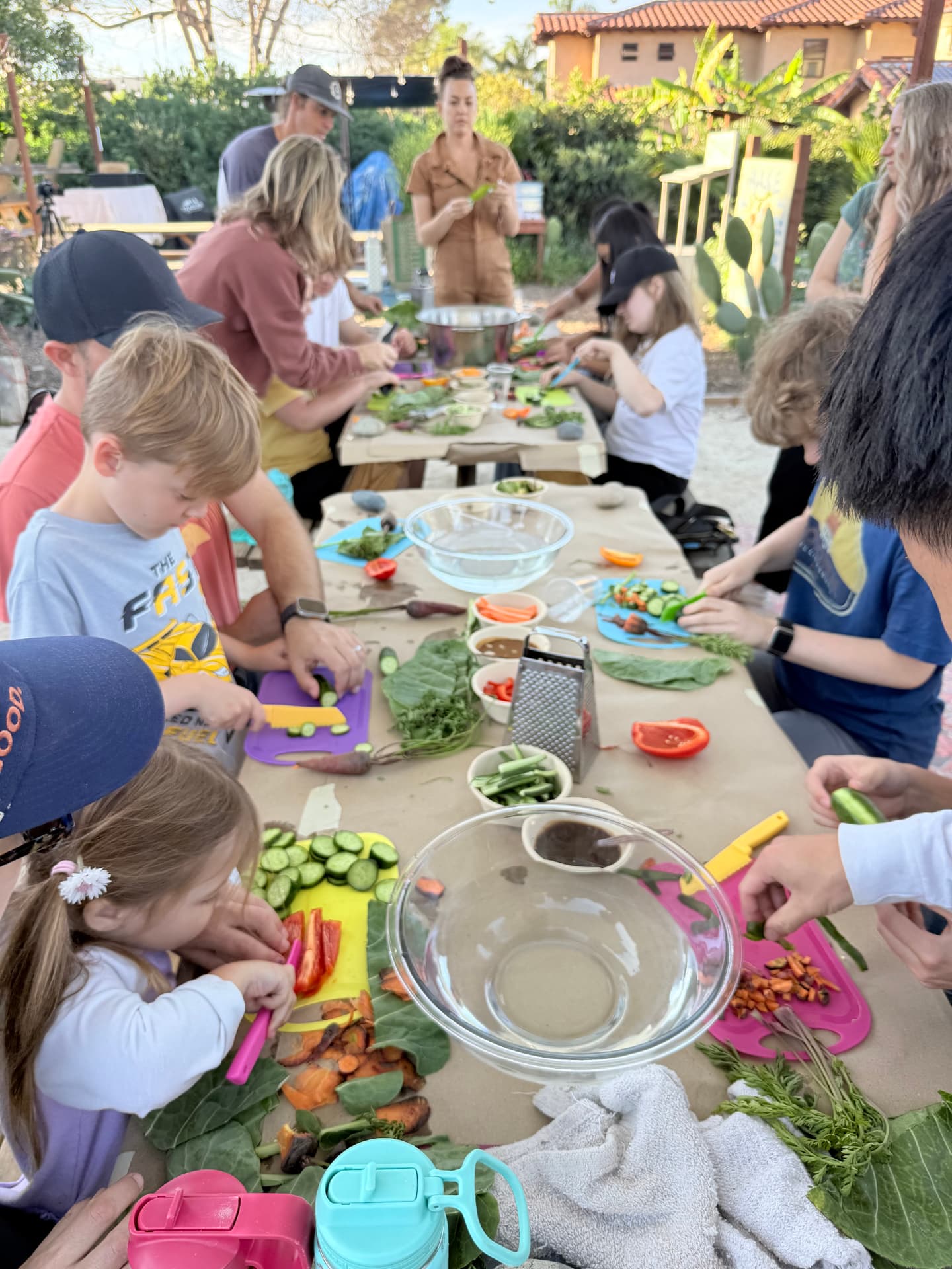Families and kids preparing fresh vegetables together at an outdoor garden table